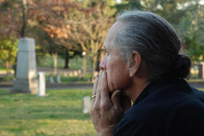 Man sitting at gravesite with a look of sadness